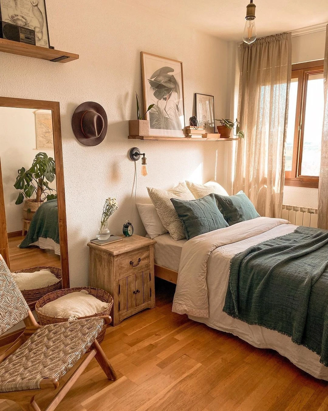 Bohemian small bedroom with green throw bed, wooden nightstand, wall shelves, woven chair, and sheer curtains.