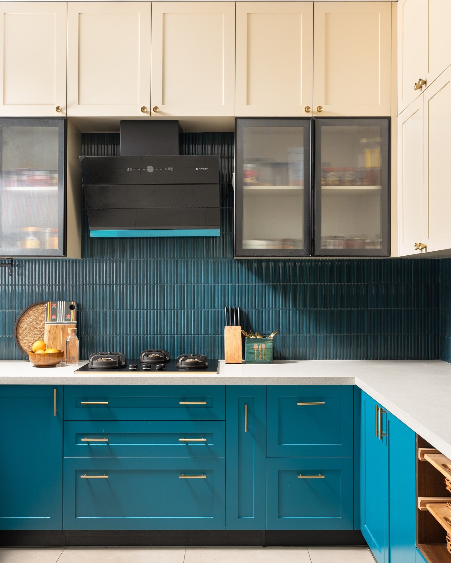 A contemporary kitchen with vibrant turquoise lower cabinets, off-white upper cabinets, and a deep blue ridged tile backsplash.