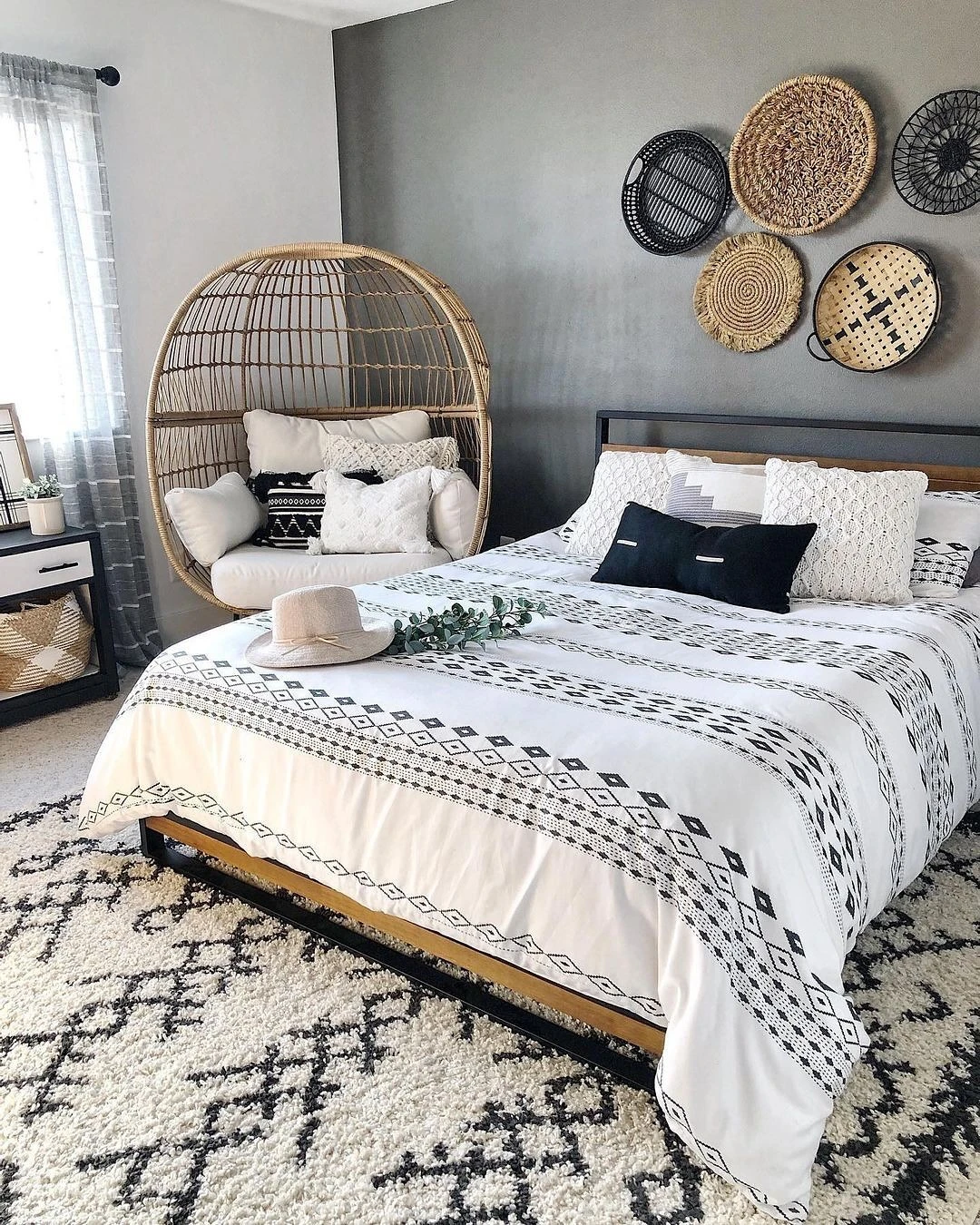 Boho small bedroom with patterned bed, hanging chair, woven baskets, potted plant, and sheer curtains.