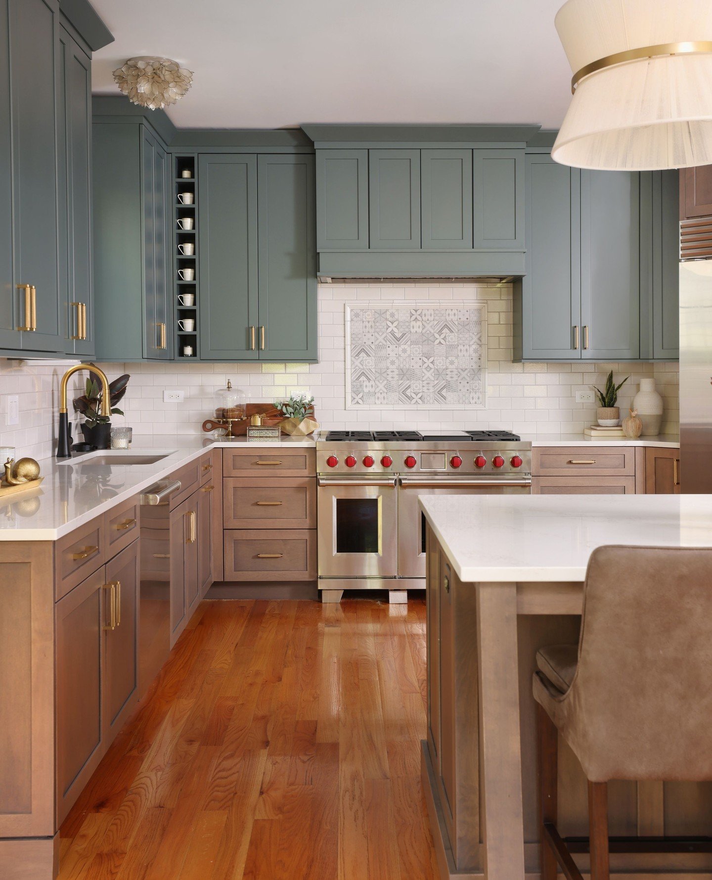 A sophisticated two-toned kitchen with gray-blue upper cabinets and warm wood-toned lower cabinets, featuring a detailed tile inlay behind the stove.