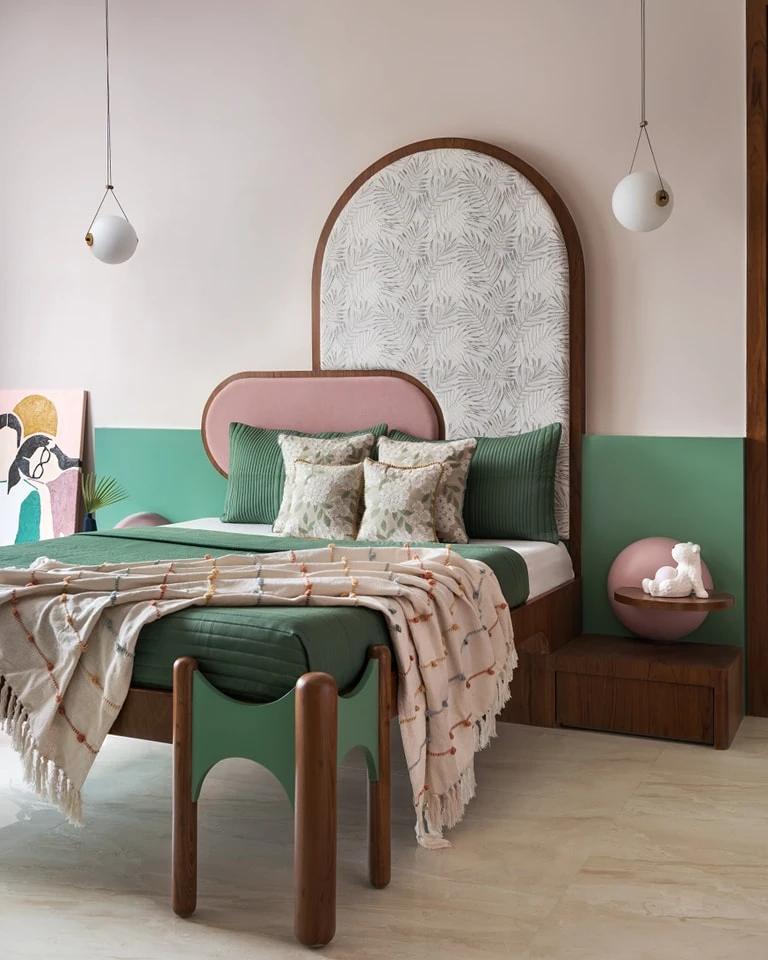 A vibrant small bedroom featuring a unique arched wooden headboard with a leaf-patterned insert and a pink trim, complemented by a two-tone pink and teal wall. Green bedding and playful decor elements create a whimsical atmosphere.