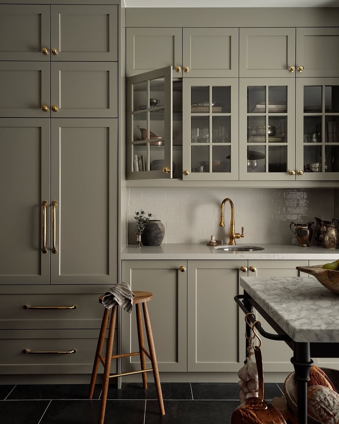A sophisticated kitchen featuring matte taupe shaker-style cabinets, a small undermount sink, and elegant brass hardware.