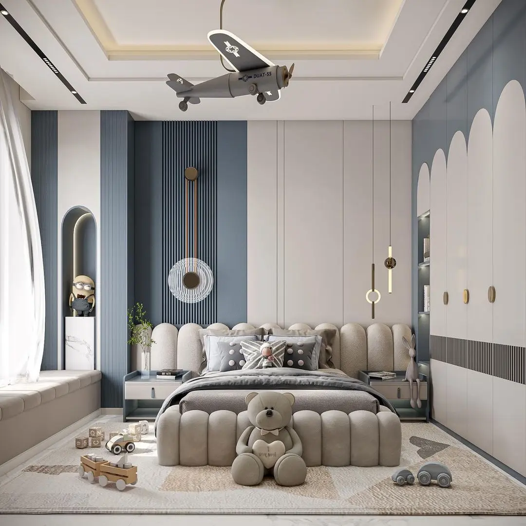 A Kid's bedroom with a neutral, soft color palette and an aviation theme. The bed features a plush, cloud-like headboard and footboard. A decorative airplane hangs from the ceiling. A built-in window seat and a large, white wardrobe with arched doors complete the modern look.