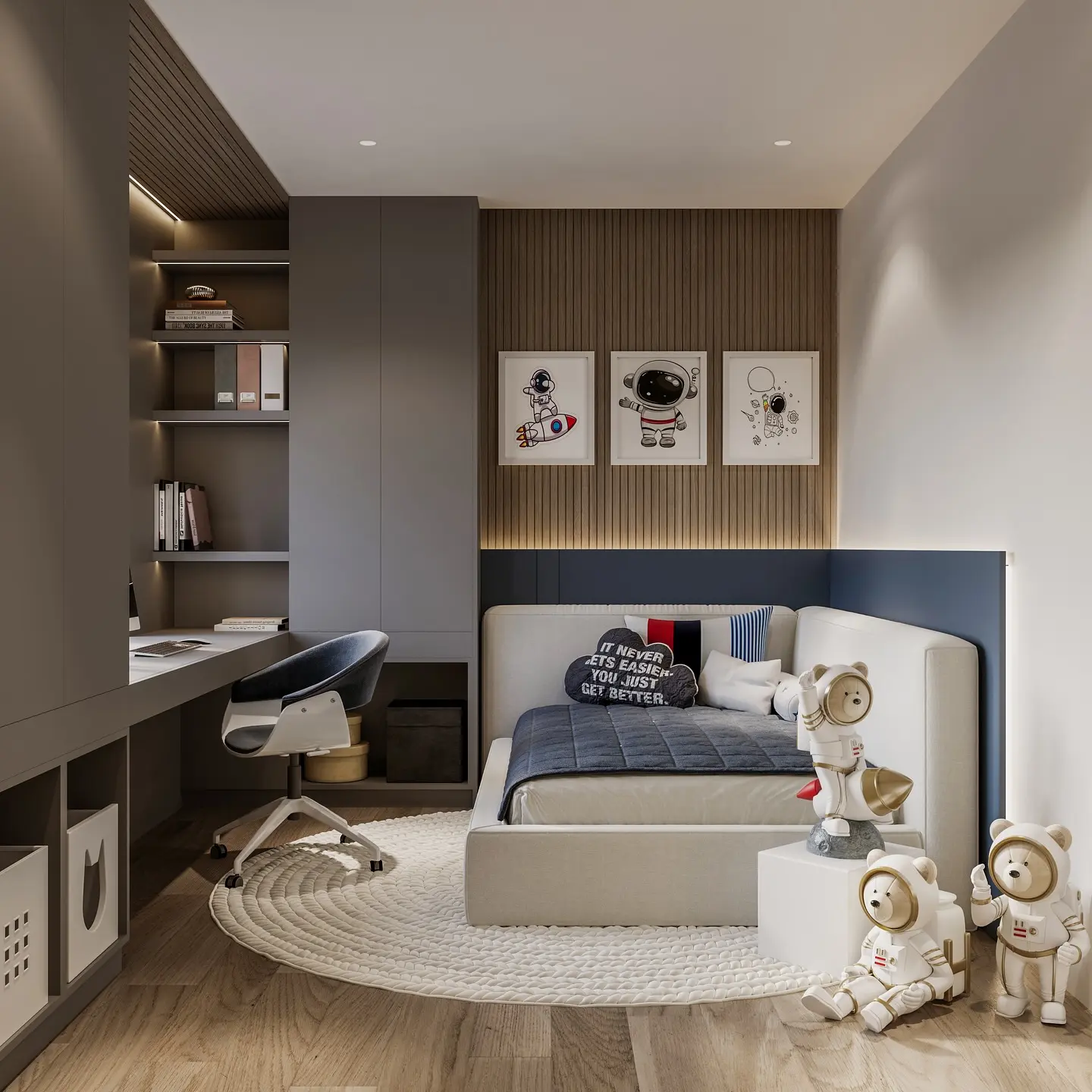 A Kid's bedroom with a space theme, featuring three framed astronaut and rocket drawings above a bed with a white upholstered headboard and a dark blue accent. The room has a long built-in desk and shelving unit with a gray finish. Astronaut figurines sit on the floor.
