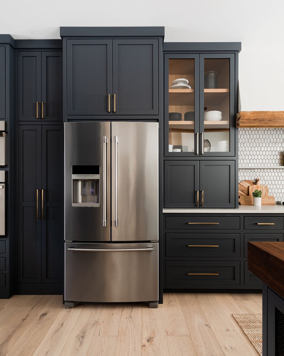 A contemporary kitchen with matte black shaker-style cabinets, a stainless steel refrigerator, and contrasting gold handles.