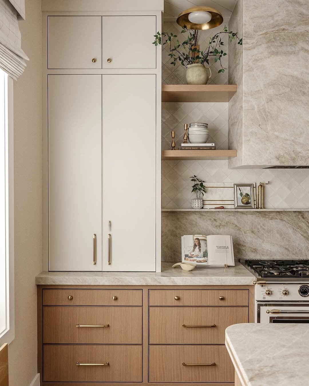 A stylish kitchen corner with light wood lower cabinets, cream upper cabinets, a marble backsplash, and gold hardware.