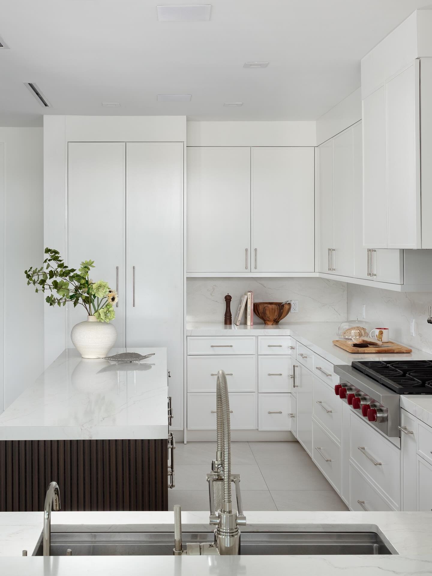 A minimalist and modern kitchen with sleek white cabinets, marble countertops, and stainless steel hardware.