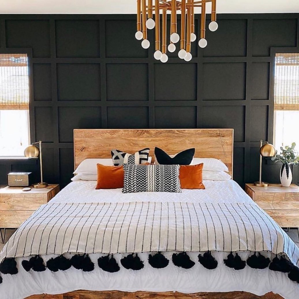 A bedroom with a black paneled accent wall, a light wood headboard, and striped bedding with black tassels.