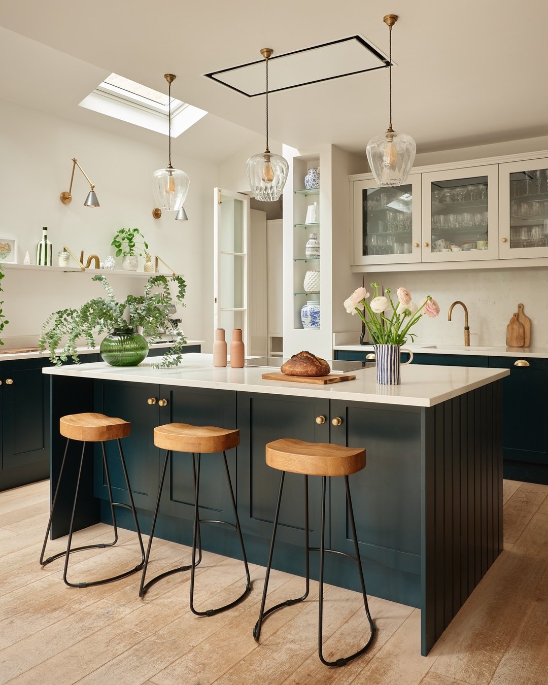 A dark blue kitchen island with a white countertop and three wooden bar stools in a bright, modern kitchen.