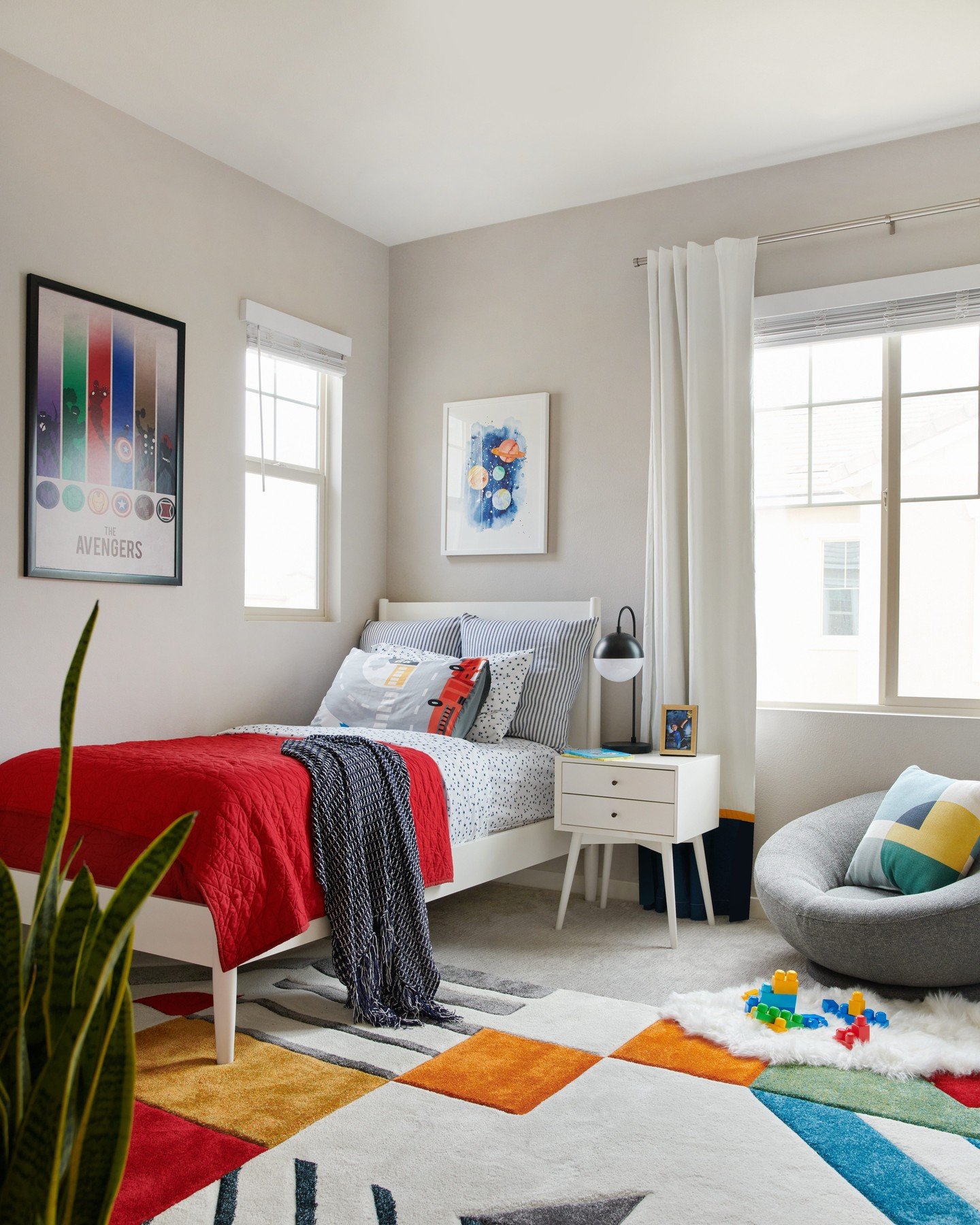 A bright, modern bedroom with a twin bed, a colorful geometric rug, and superhero-themed decor.