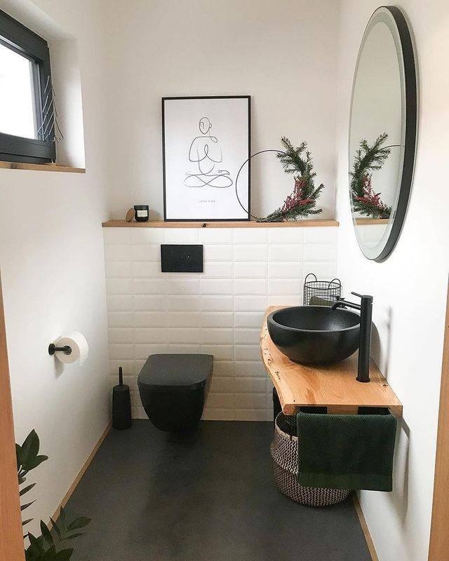 A tiny powder room with white walls, a floating live-edge wood vanity, a black vessel sink, and a circular mirror with a black frame.