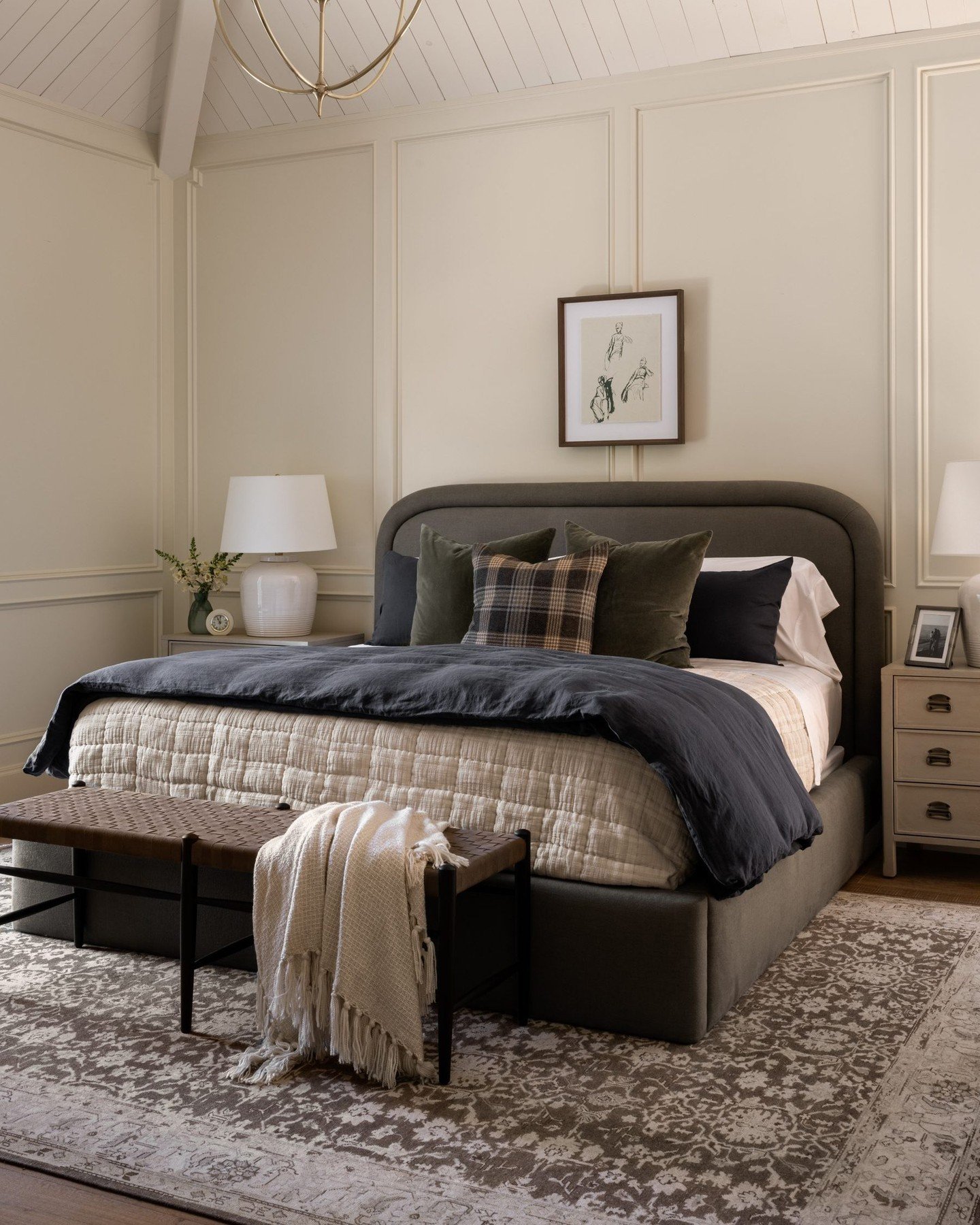 A bedroom with a paneled accent wall, a dark upholstered bed, and a plaid pillow.