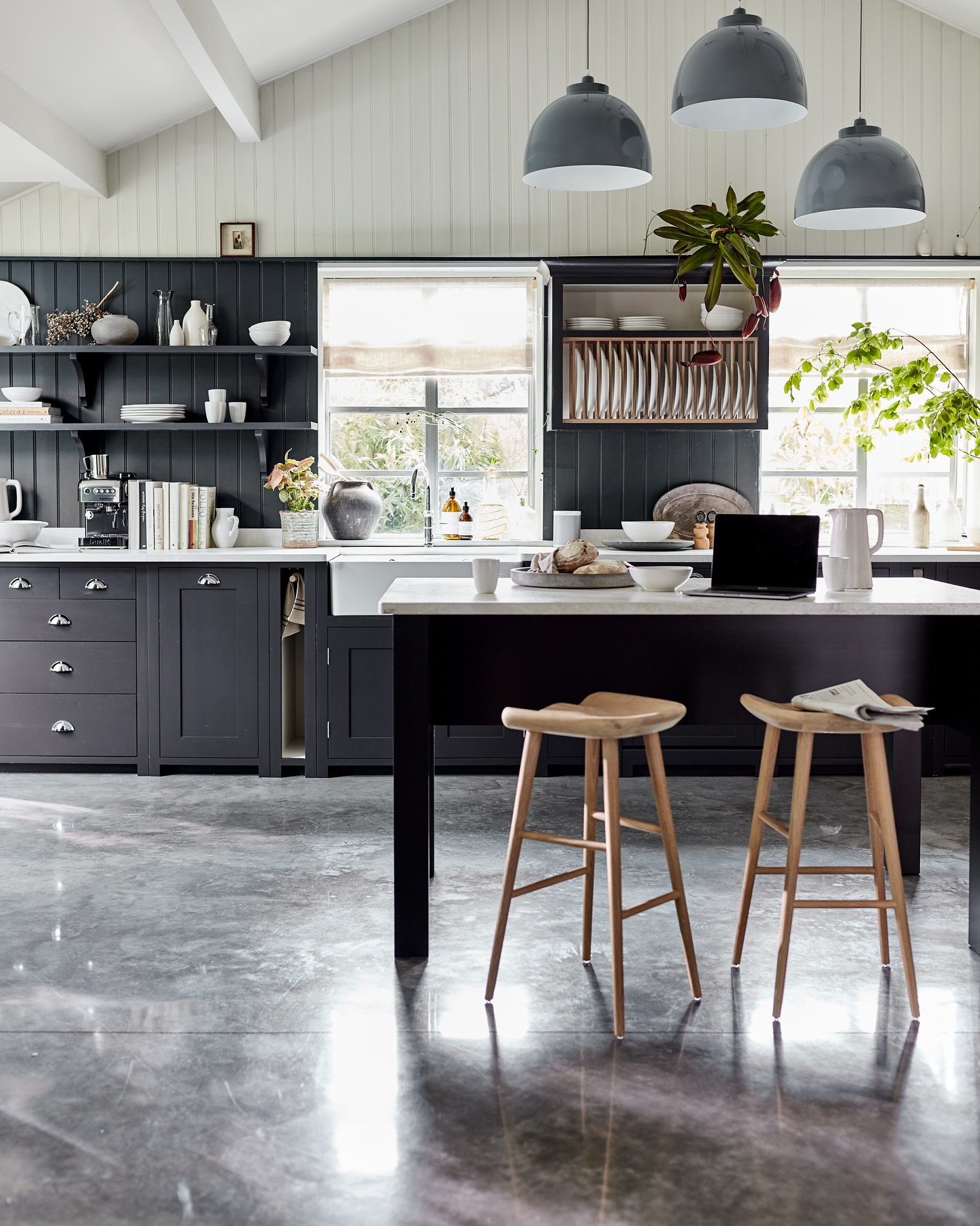 A dark blue kitchen island with a white countertop and two wooden bar stools in a rustic, light-filled kitchen with a vaulted ceiling.