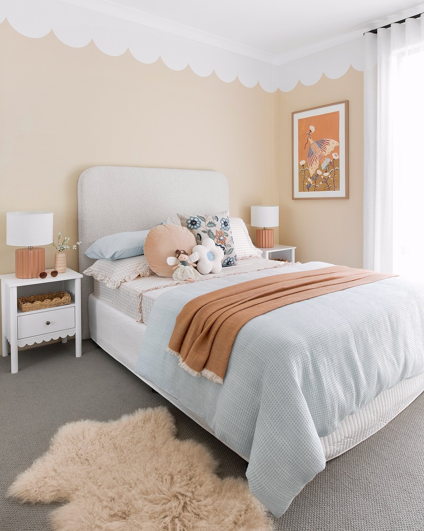 A cozy teen girl's bedroom with a soft pastel color scheme, featuring a scalloped wall detail and whimsical art.