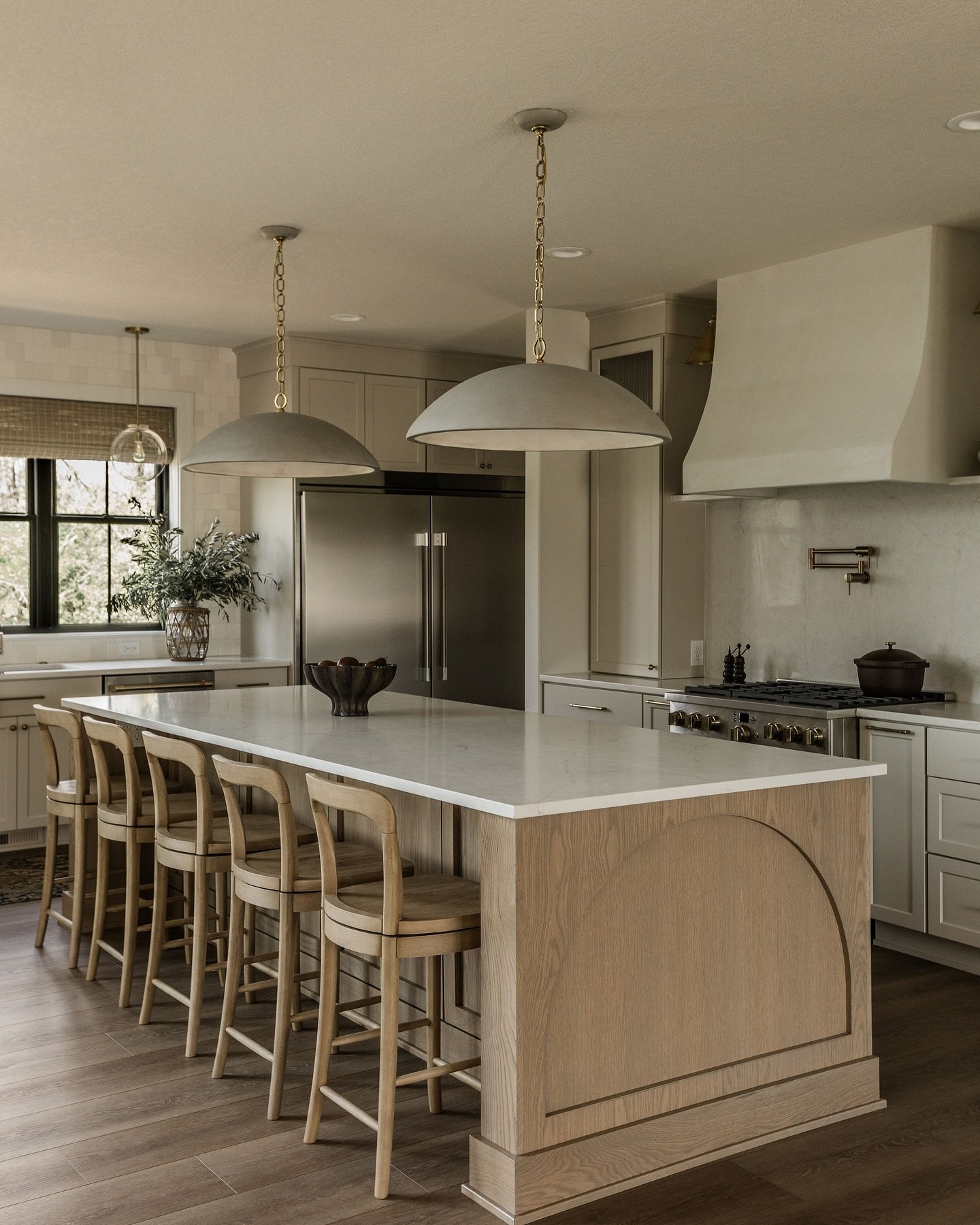 A large, light wood kitchen island with a white countertop, featuring an arched side panel and five matching wooden bar stools.