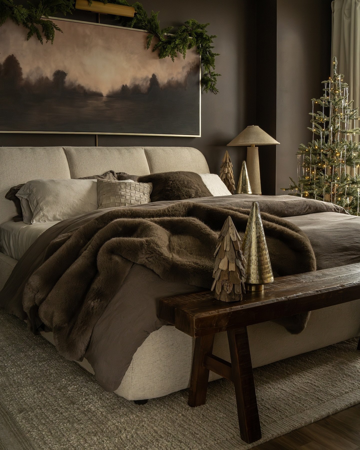 A bedroom with a neutral bed, dark walls, and a fluffy brown faux fur blanket.