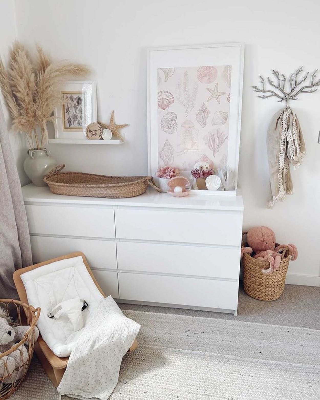 A cozy corner of a nursery with a white dresser, a large framed print of seashells, and coastal-themed decor.
