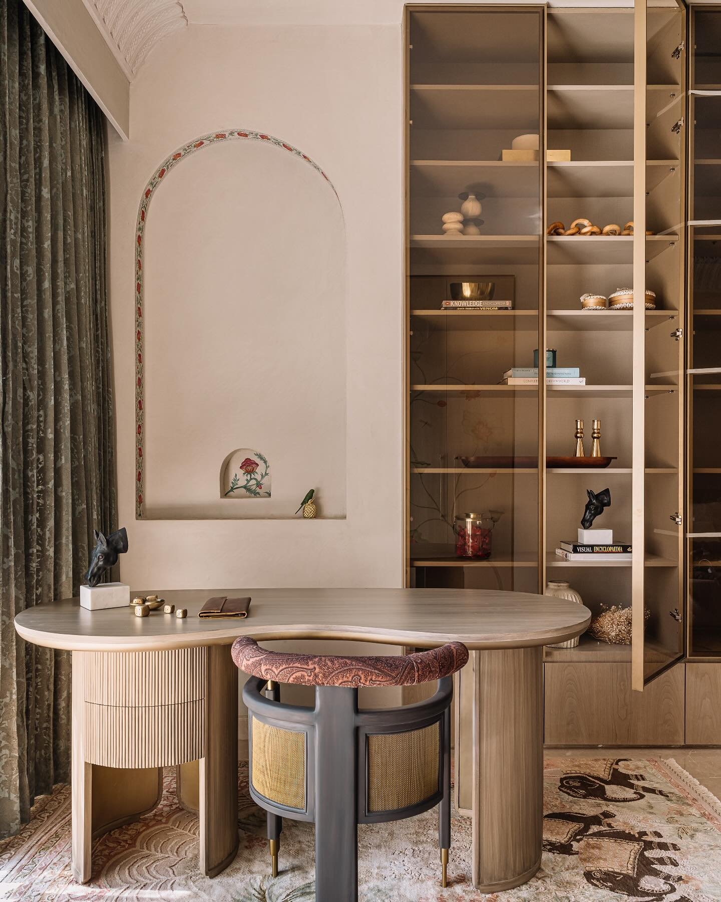 An organic-shaped wooden study desk with a fluted pedestal and a drawer unit, paired with a stylish chair with a patterned cushion.