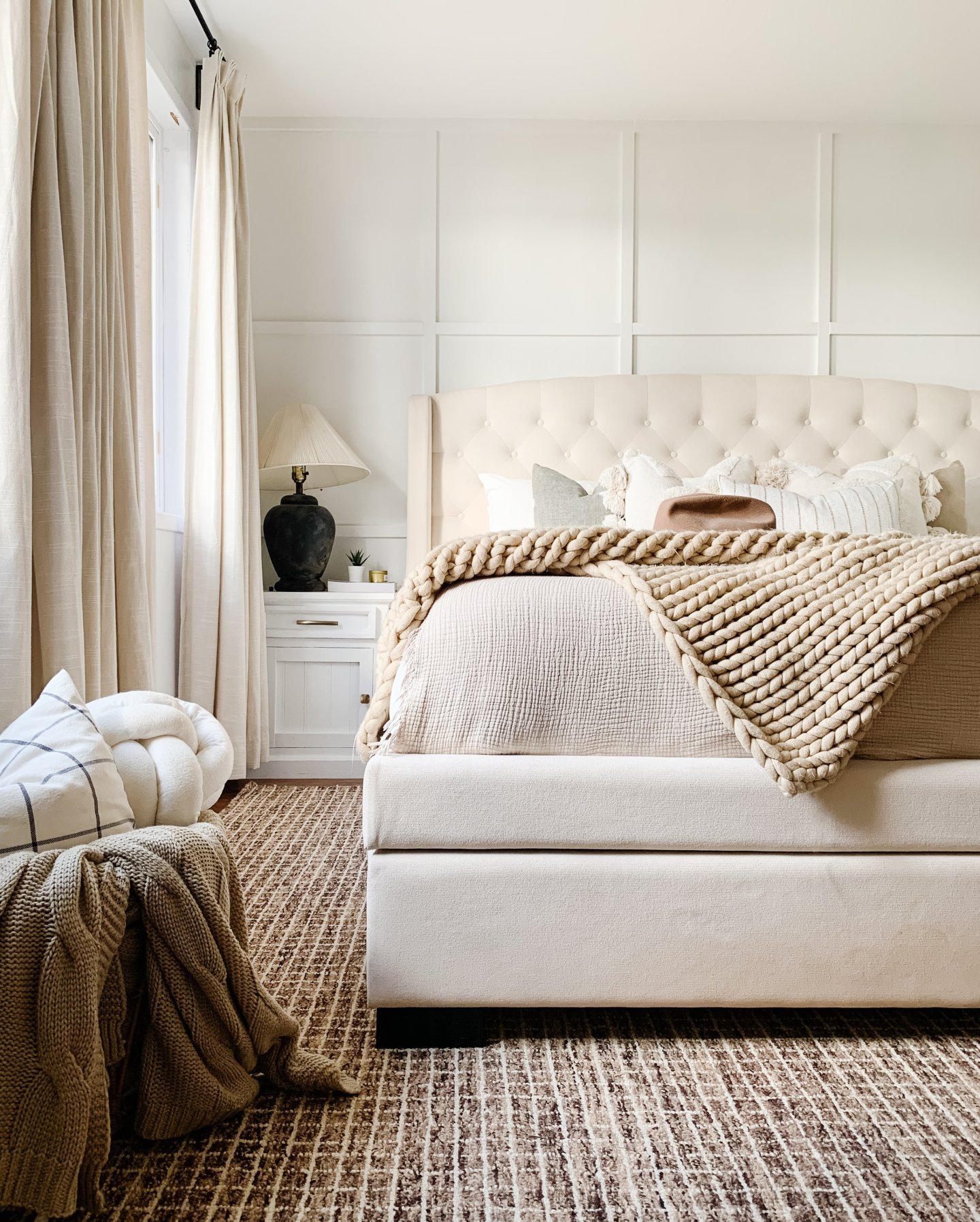 A large, natural fiber area rug with a woven grid pattern in shades of brown and beige is placed under a large, light-colored bed.