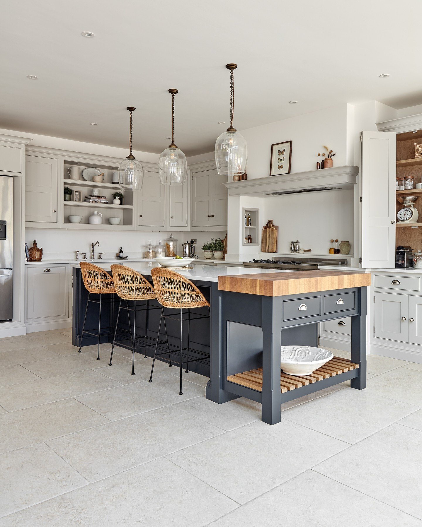 A two-part kitchen island with a dark gray section for seating and a separate dark gray butcher block on wheels, featuring rattan bar stools.