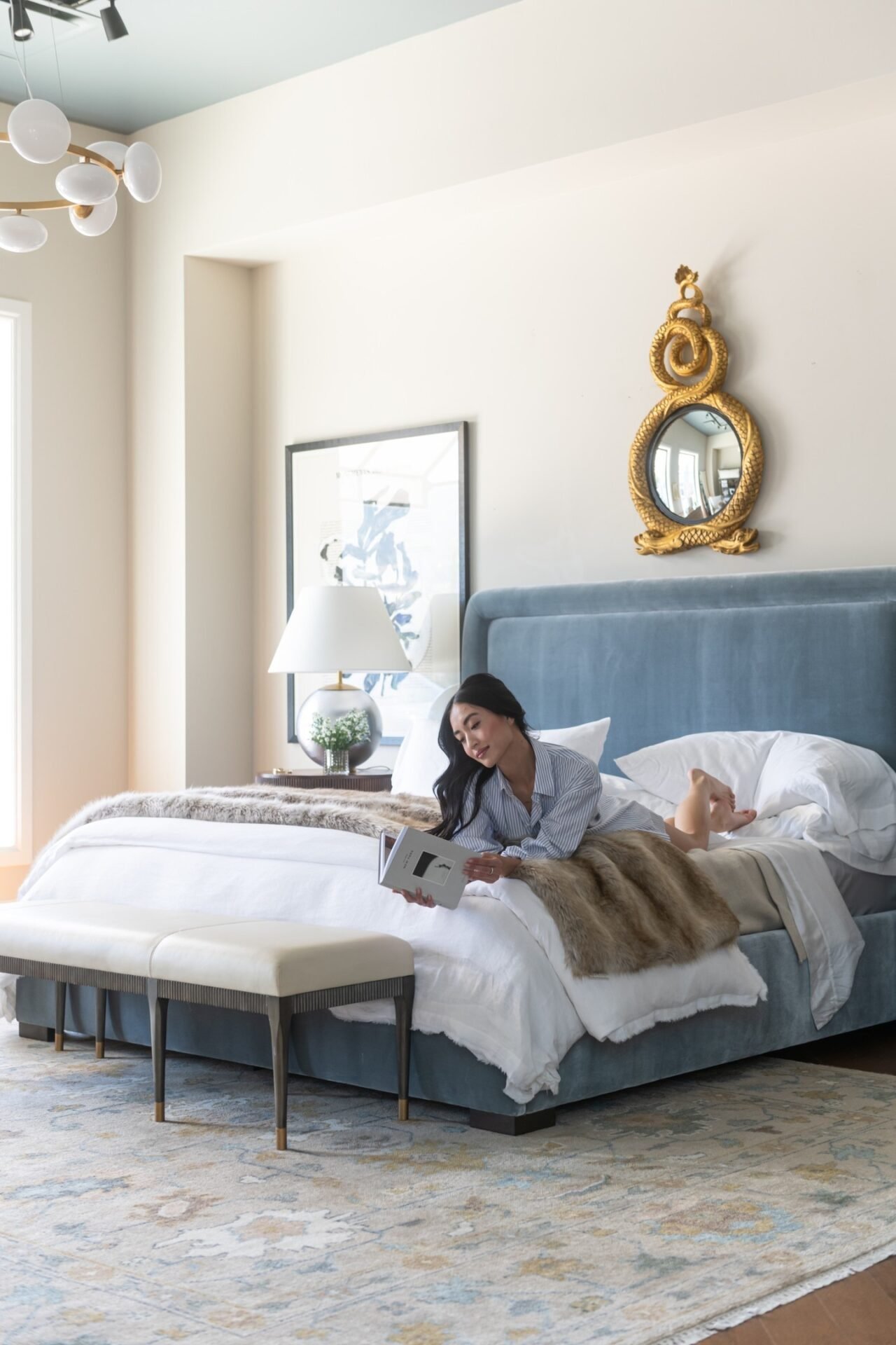 A large, faded area rug with a distressed pattern in light gray, beige, and blue is placed under a bed with a blue upholstered headboard.