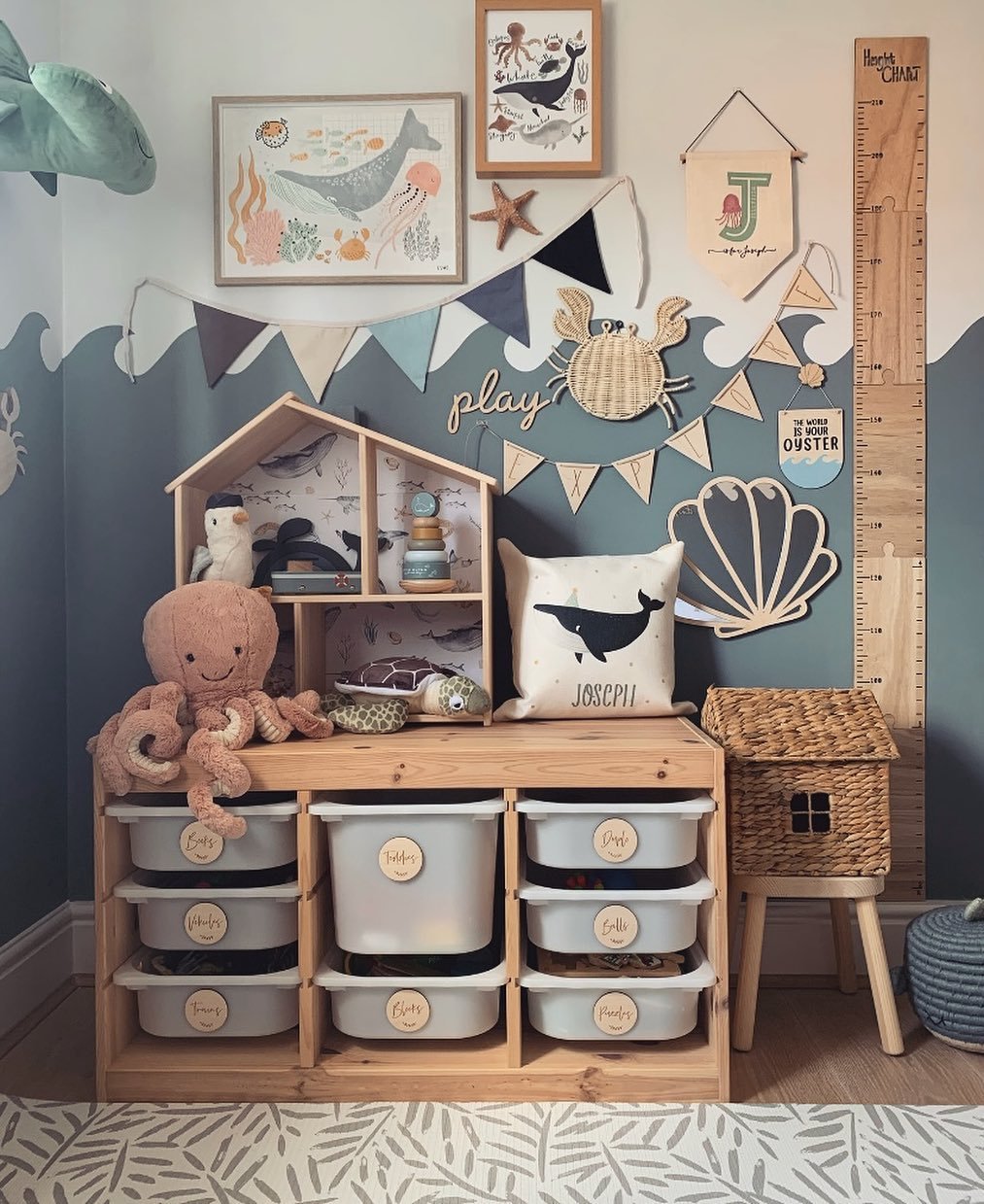 A child's playroom with a two-toned wall, a wooden storage unit, and various ocean-themed decorations like a crab, shell, and sea animal art.