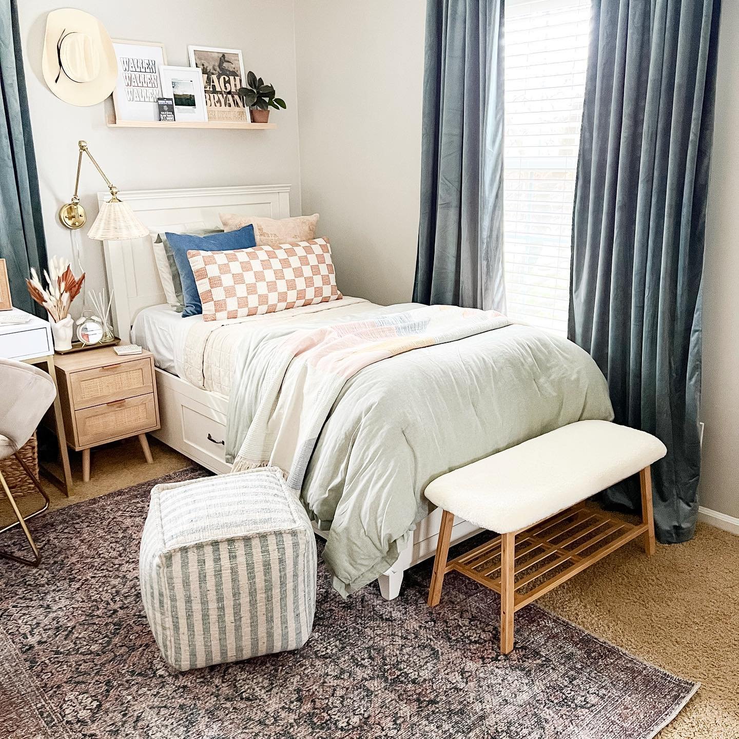 A teen's bedroom with a farmhouse and bohemian mix, featuring a white bed, a wooden floating shelf, and dark teal curtains.