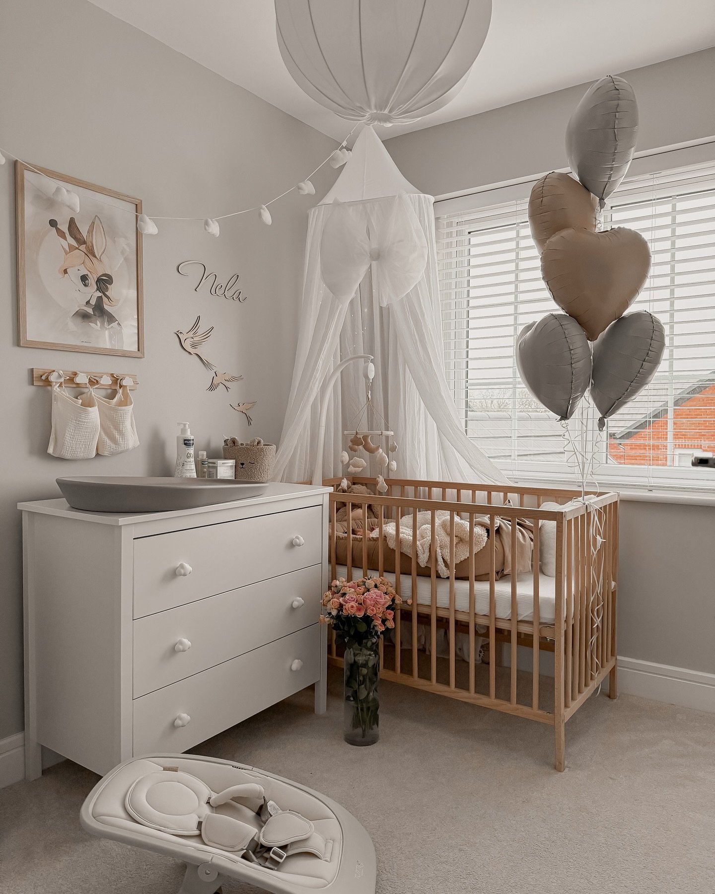 An elegant and whimsical nursery with a wood crib, a white canopy, heart balloons, and a white dresser.