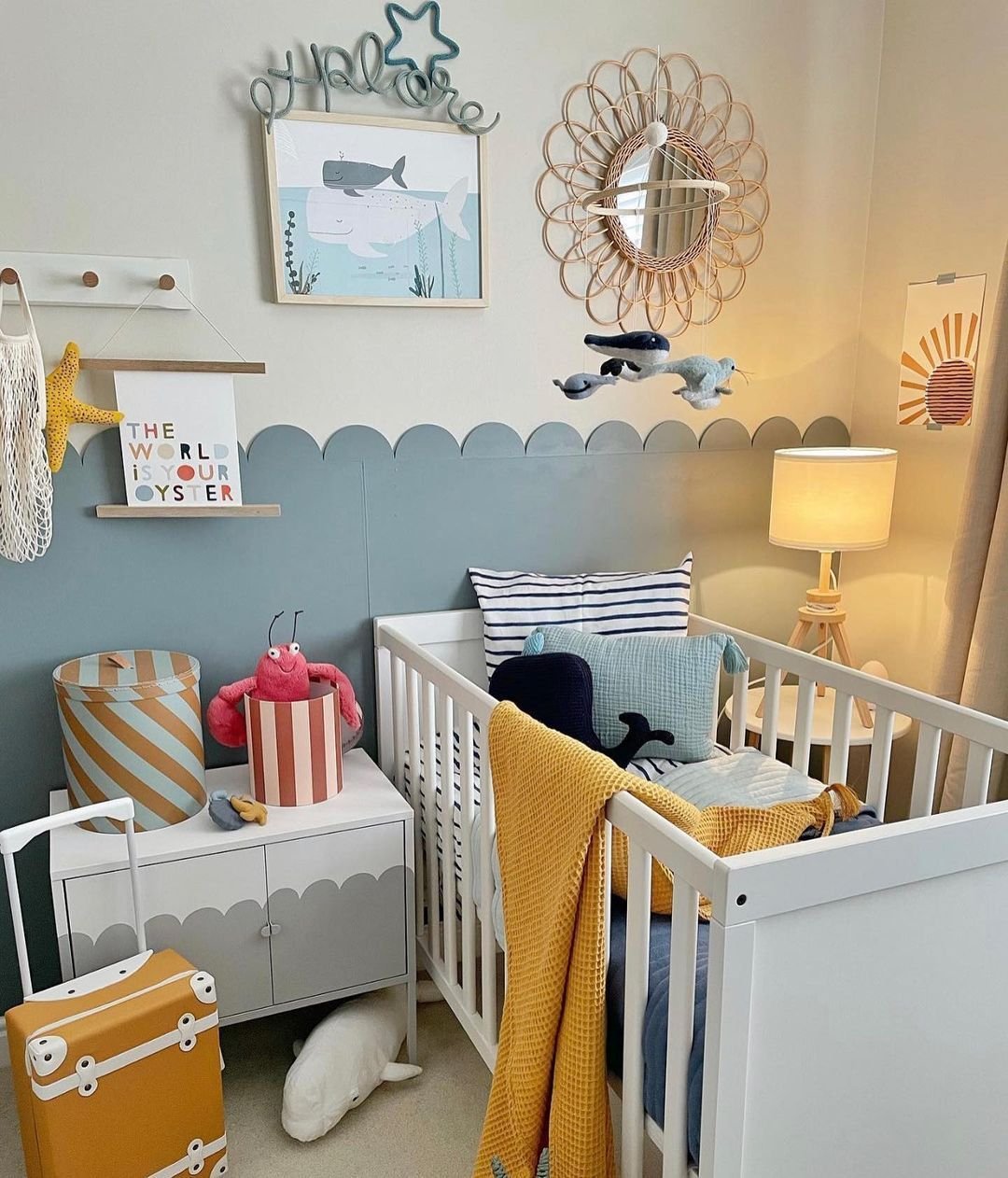 A nursery with a white crib, a scalloped two-toned wall, and whimsical ocean-themed decor including a lobster toy and whale art.