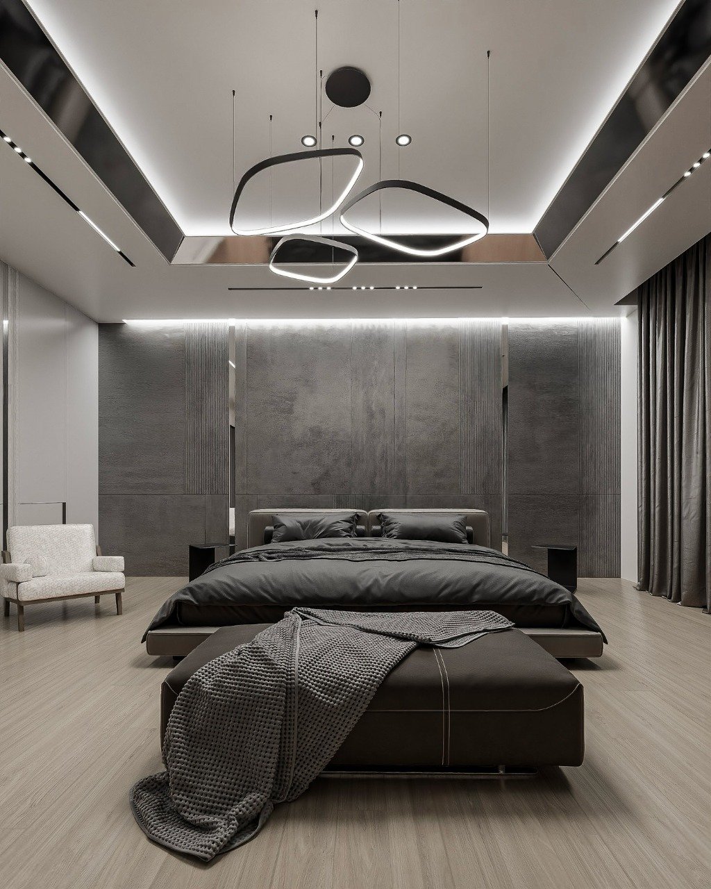 A dark, moody bedroom with a low-profile bed, an oversized leather ottoman, and a headboard wall made of dark concrete-like panels. The room features a dramatic, multi-piece abstract chandelier.