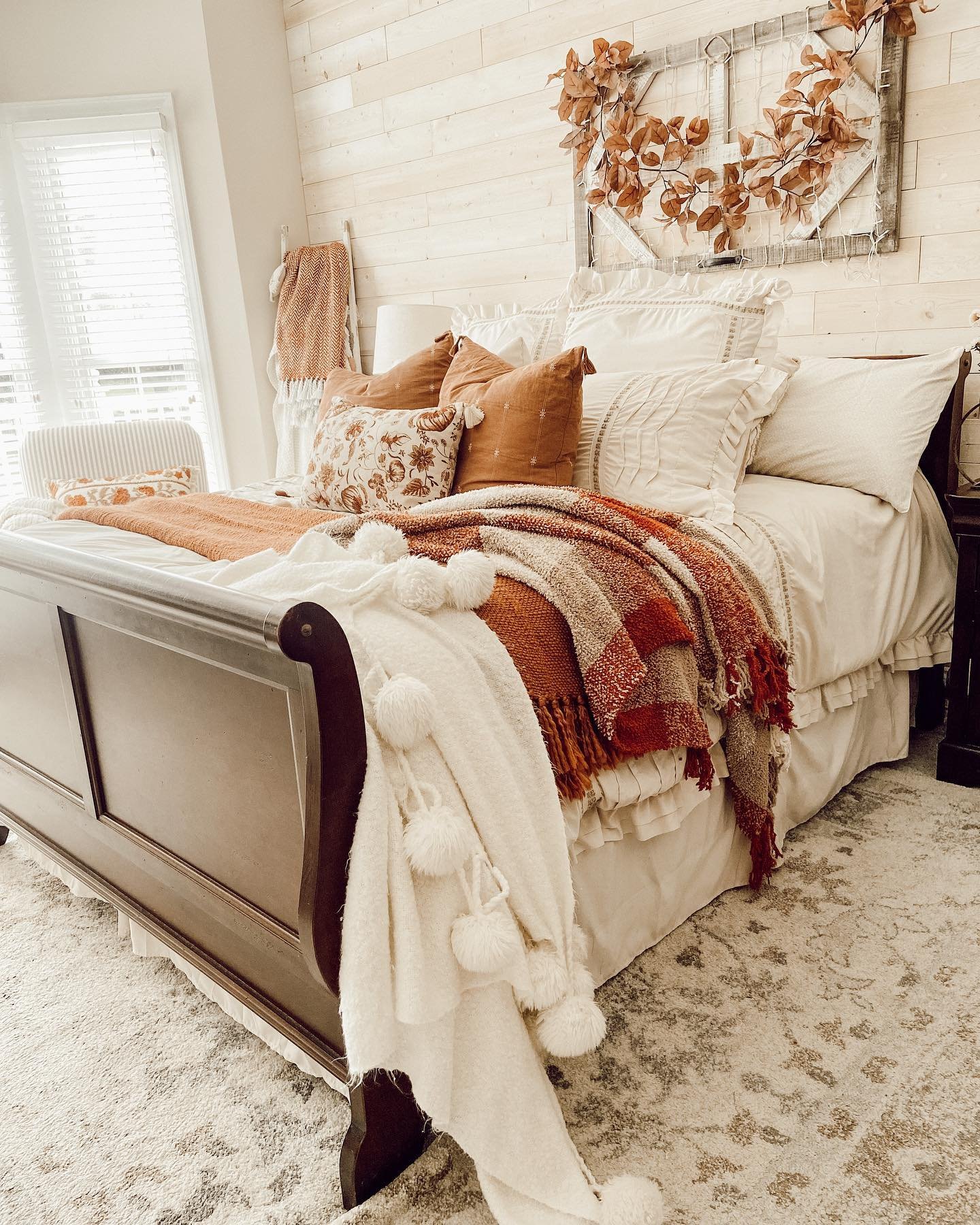 A bedroom with a white shiplap wall, a dark wood sleigh bed, and layered blankets in warm, earthy colors.