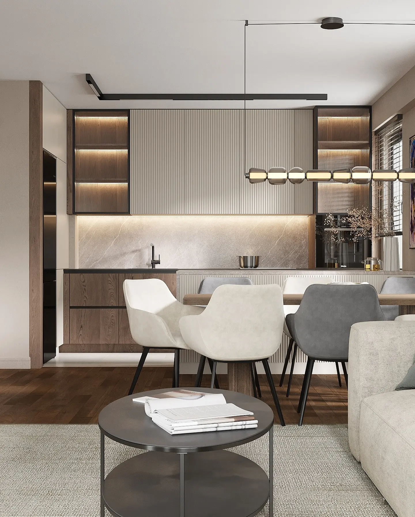 A view of a compact, modern open-concept space. The living area is in the foreground with a round coffee table and a sofa. The dining area features a wooden table with mixed-style chairs. The kitchen has a textured vertical panel backsplash, open shelving, and a marble countertop.