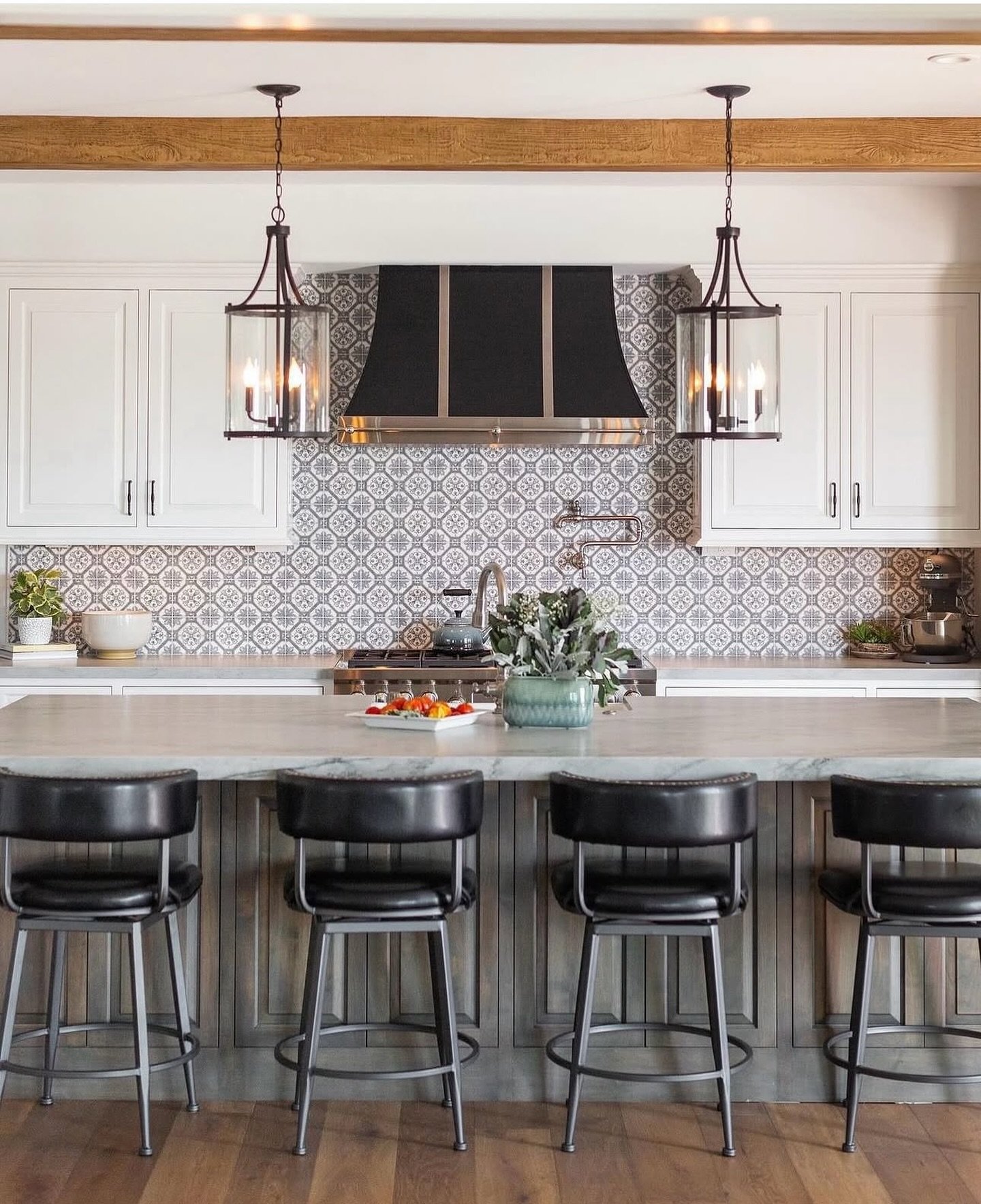 A kitchen featuring a backsplash with a repeating floral and geometric pattern in shades of gray and white, complementing white cabinetry, a large island, and industrial-style pendant lights.