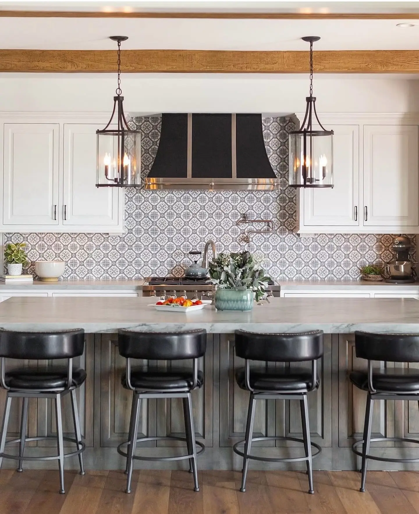 A kitchen featuring a backsplash with a repeating floral and geometric pattern in shades of gray and white, complementing white cabinetry, a large island, and industrial-style pendant lights.
