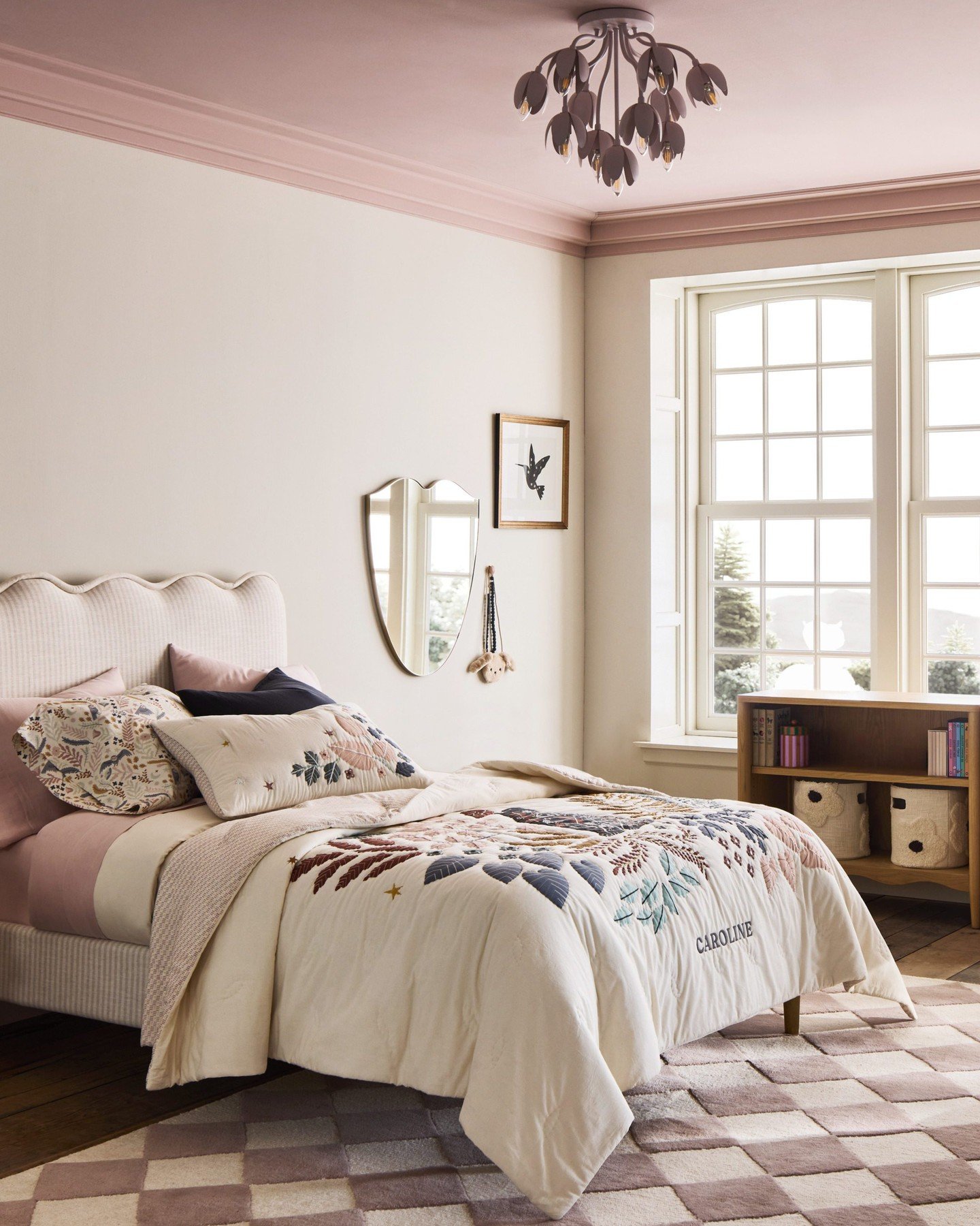 A child's bedroom with a scalloped headboard, a floral-patterned comforter, and pink and beige accents.