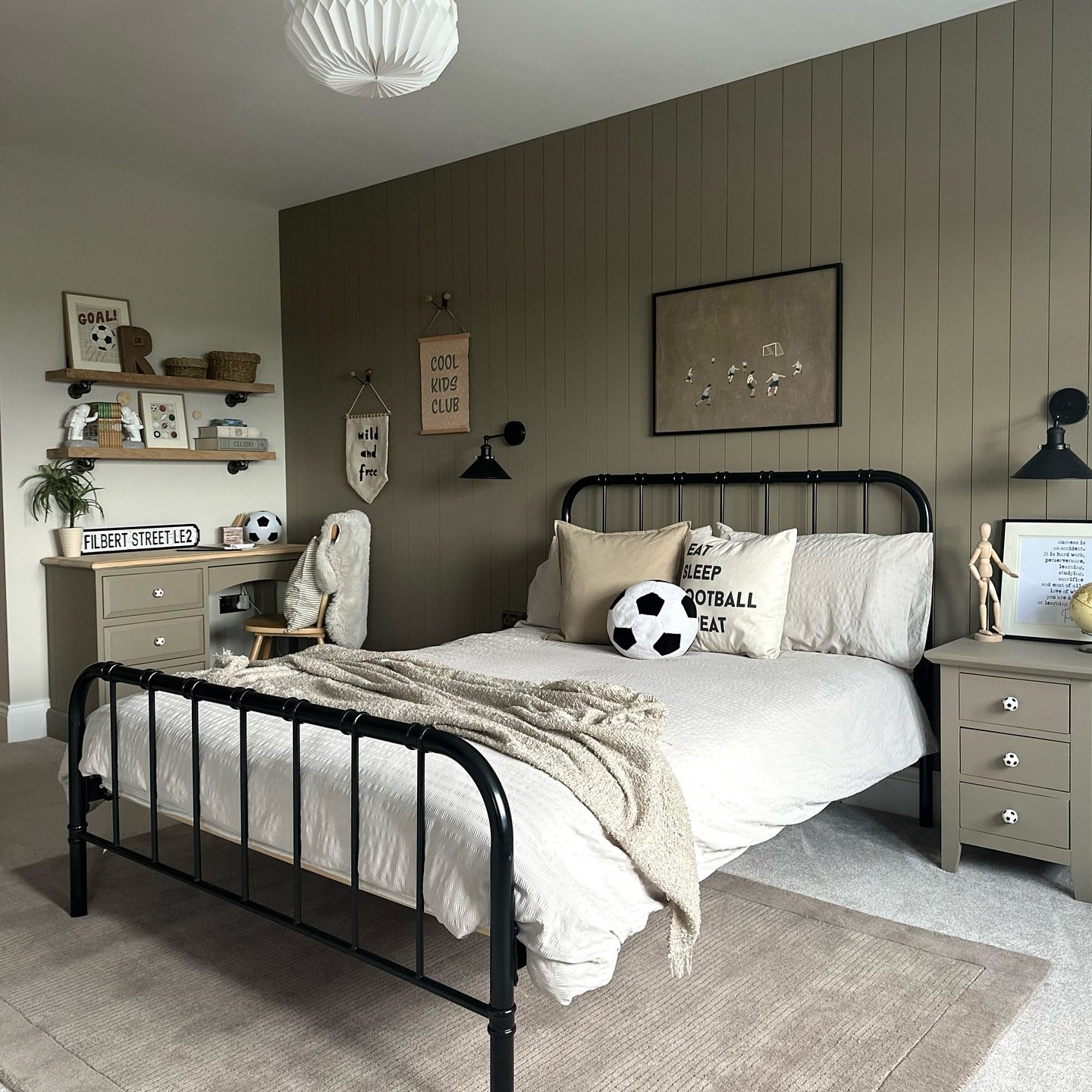 A bedroom with a vertical wood-paneled accent wall, a black metal bed frame, and subtle football-themed decor.