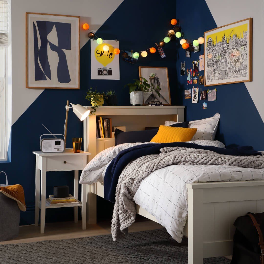 A vibrant teen bedroom with a geometric blue and white accent wall, a white bed with built-in shelving, and colorful string lights.