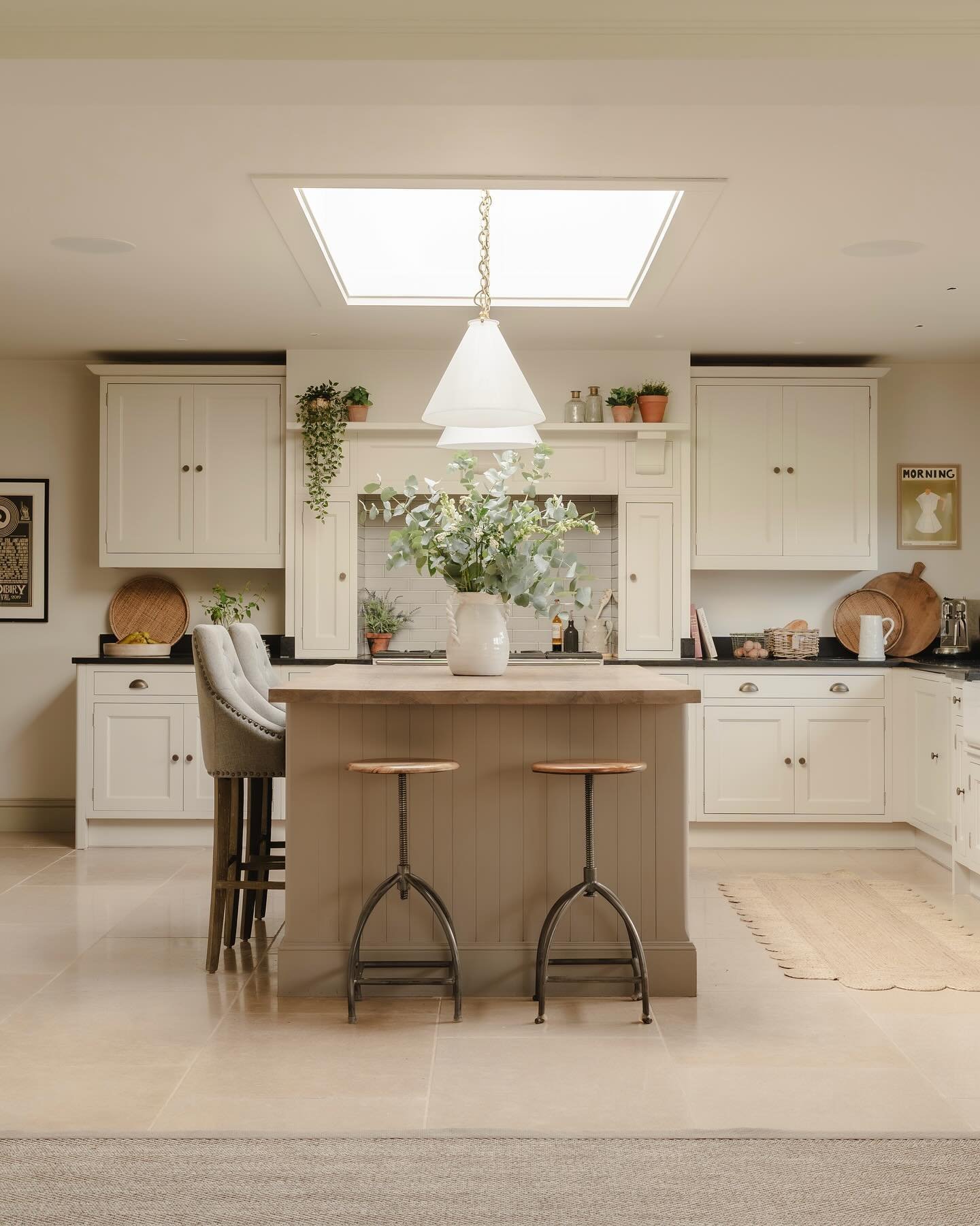 A small, square kitchen island with a light wood countertop, a beige base, and a mix of bar stools in a light and airy kitchen.