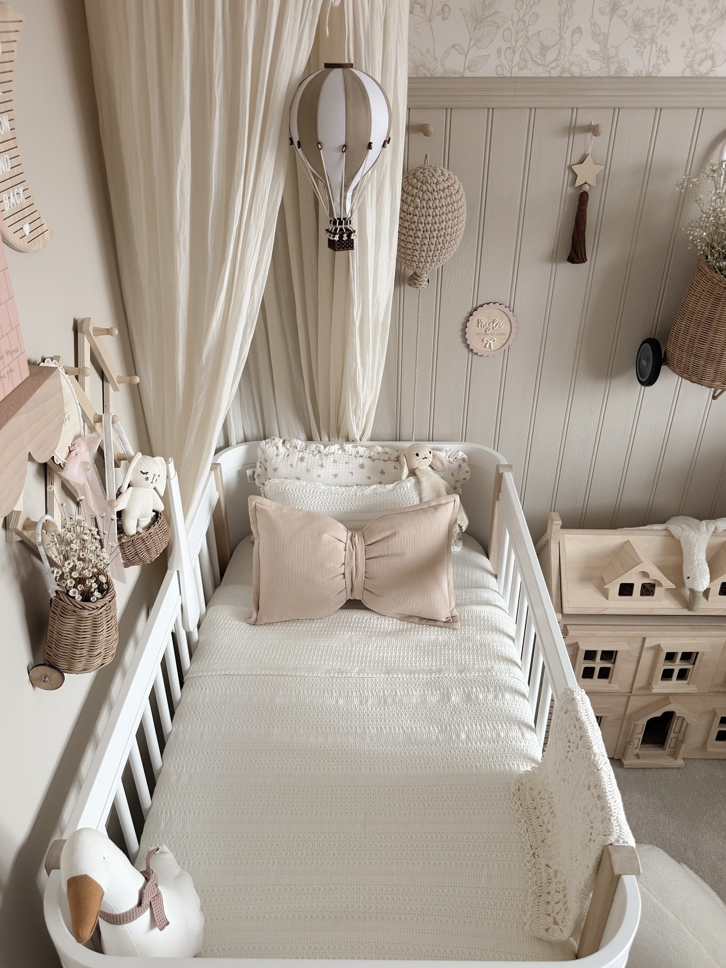 A cozy toddler room with a white crib, a large bow pillow, and a hot air balloon light fixture.