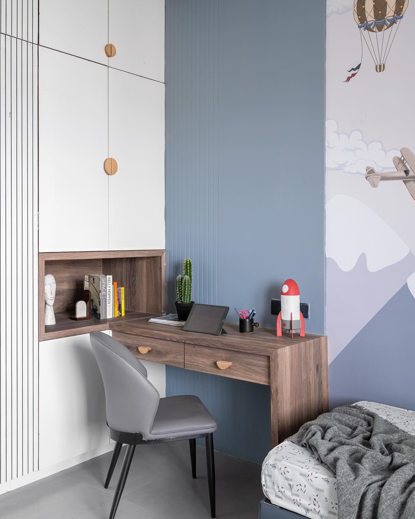 A modern, floating wooden study desk with two drawers, a built-in shelf above, and a sleek gray chair in a child's room.