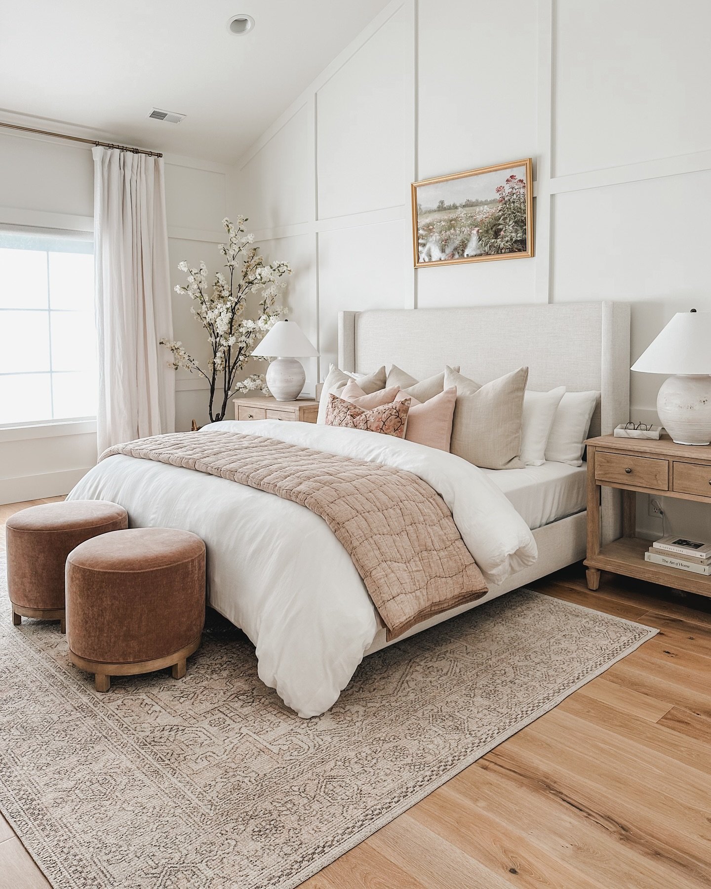 A large area rug with a soft, traditional pattern in beige and cream is placed under a bed with a light-colored headboard and bedding.