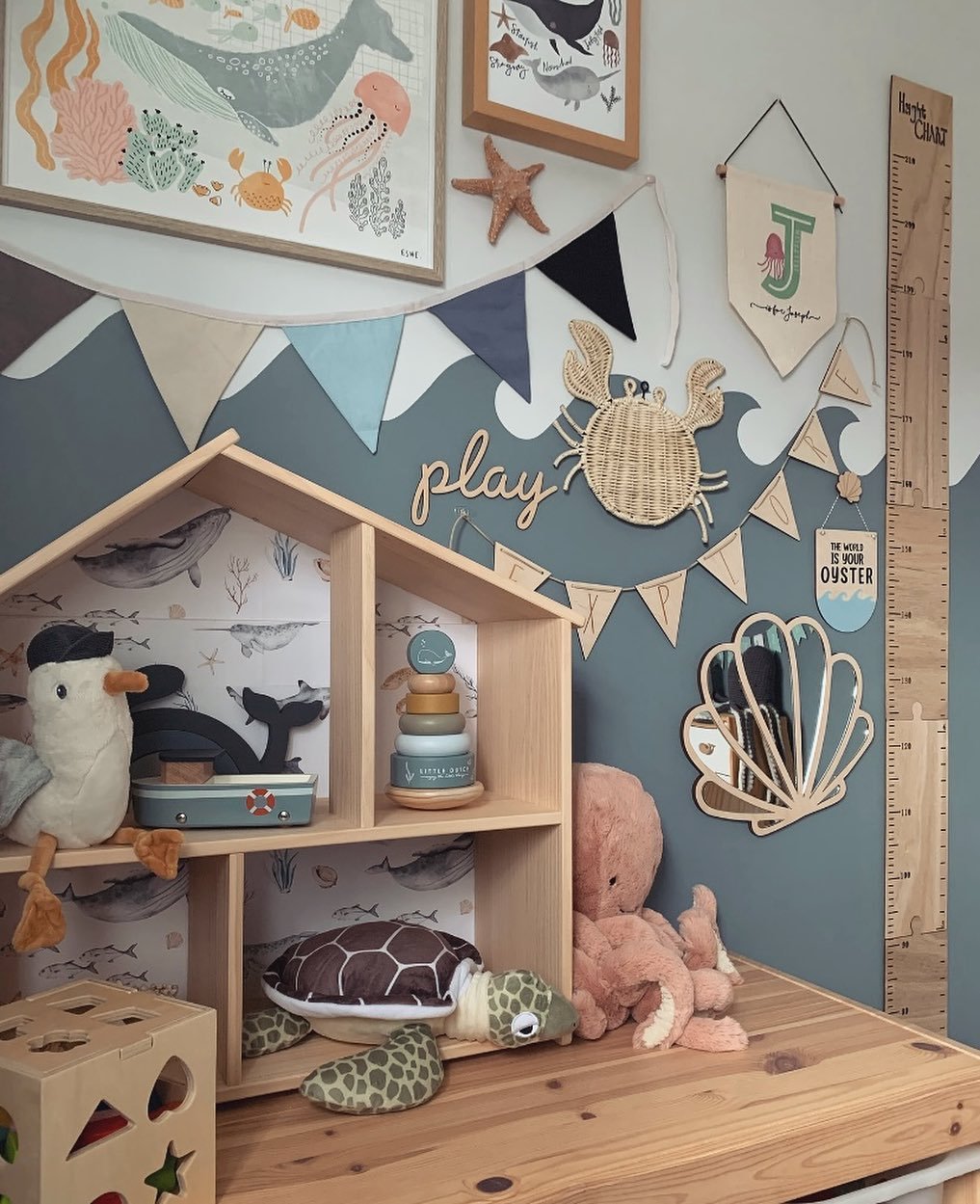 A child's play corner with a wooden dollhouse, a two-toned wave wall, a variety of sea animal toys, and framed art.