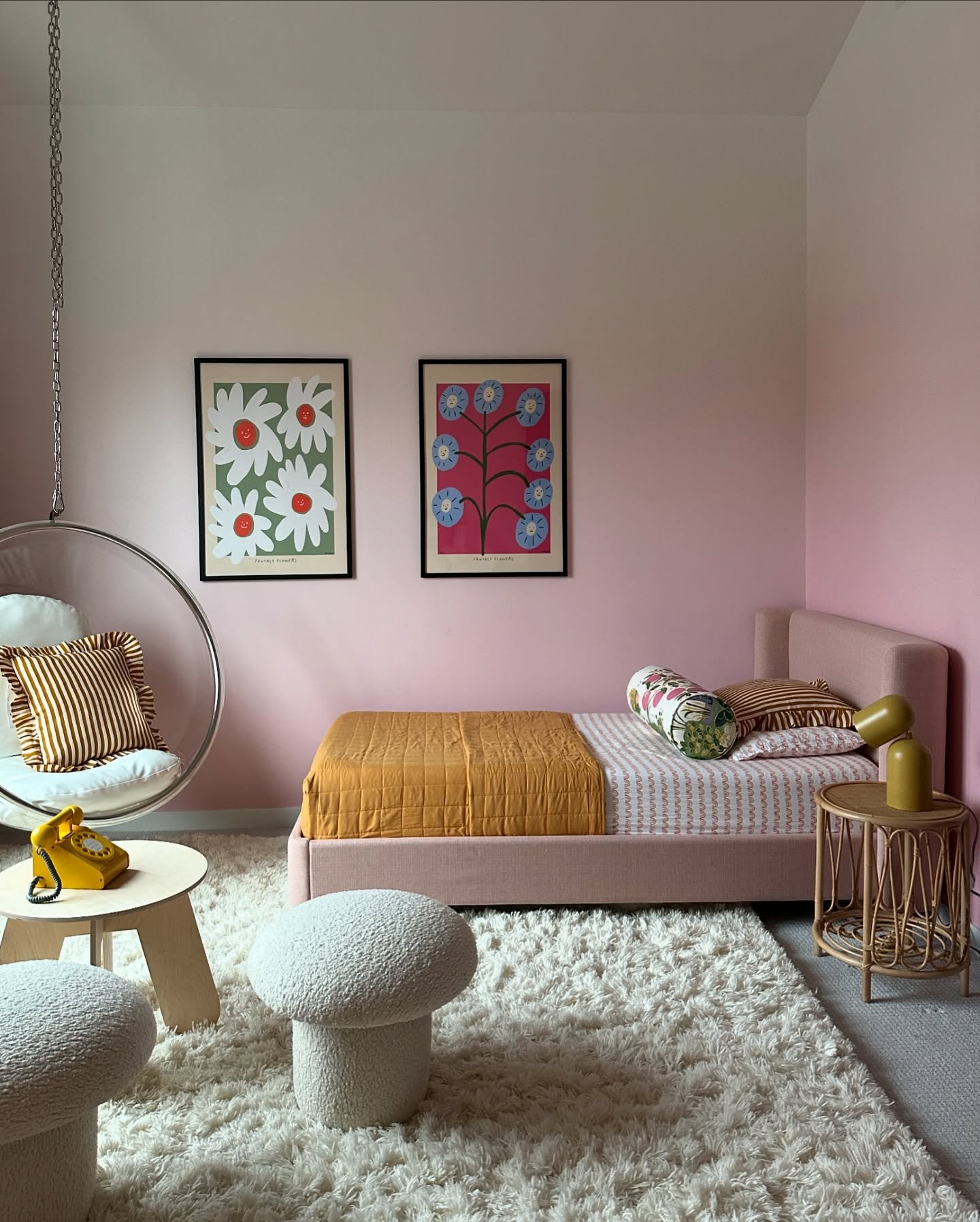 A playful bedroom with pink ombre walls, a hanging bubble chair, and retro-style mushroom stools and wall art.