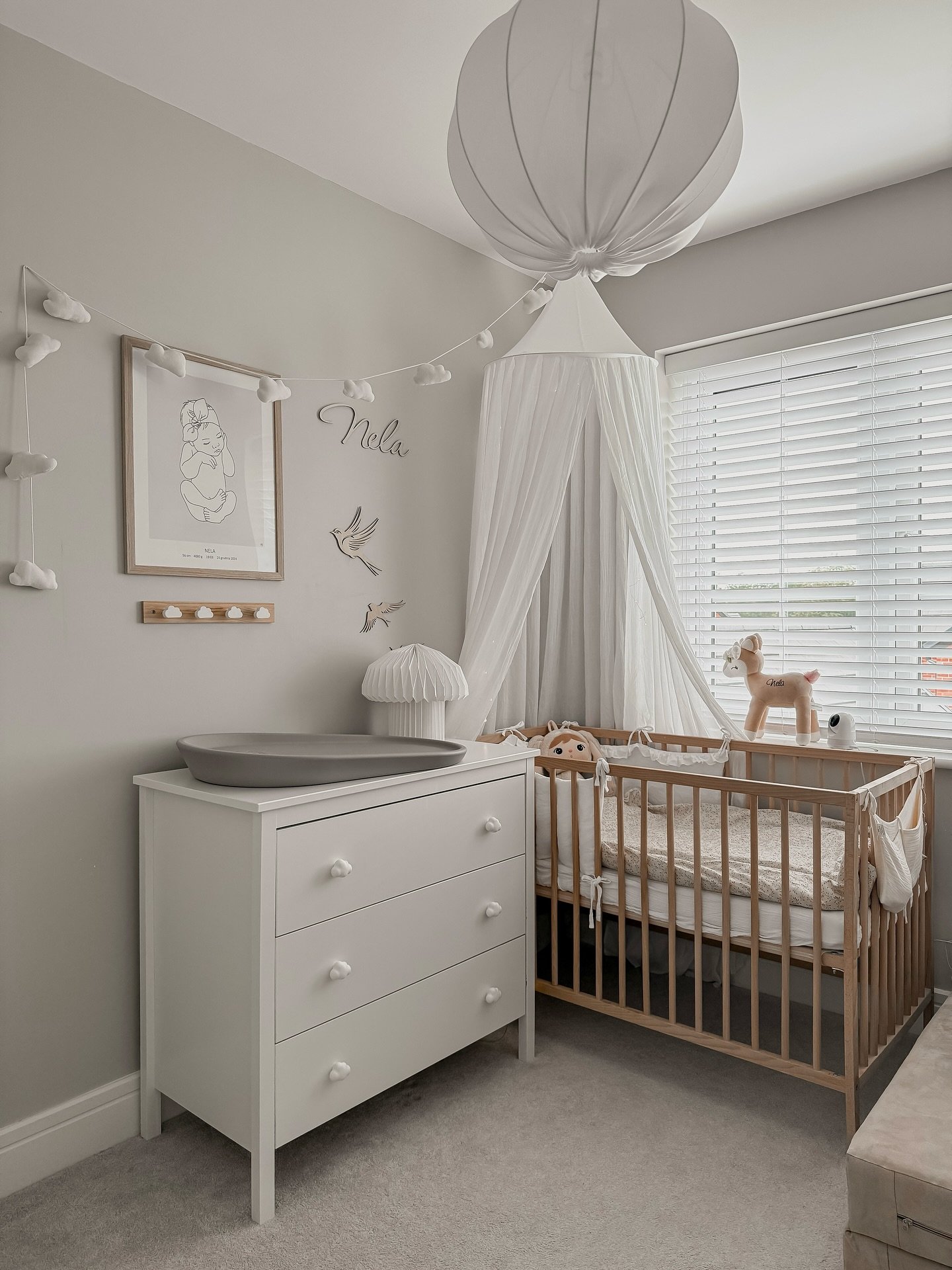 A serene nursery with a wood crib under a canopy, a white dresser, and a baby line art print.