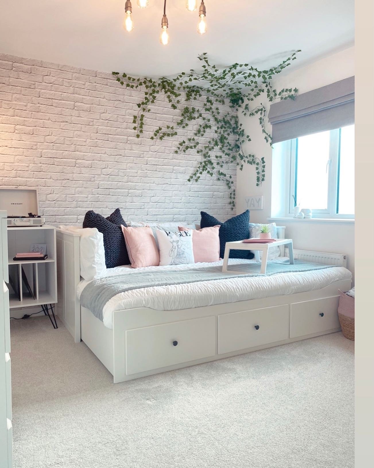 A cozy teen's bedroom with a white brick accent wall, a daybed with built-in storage, and faux ivy decor.