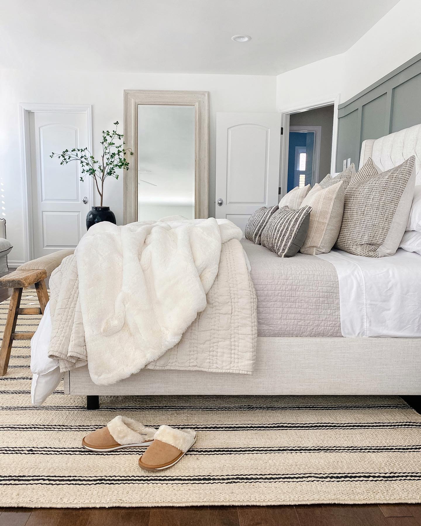 A bright bedroom with a white upholstered bed and a fuzzy blanket draped over the end.