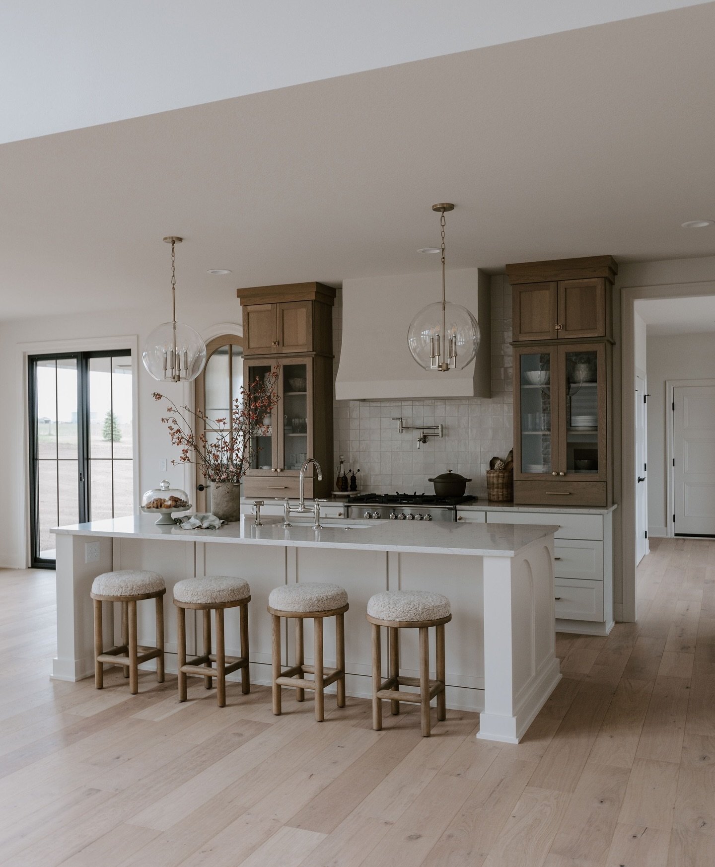 A large white kitchen island with a white countertop and four wooden bar stools with fluffy white seats in a bright, modern farmhouse kitchen.