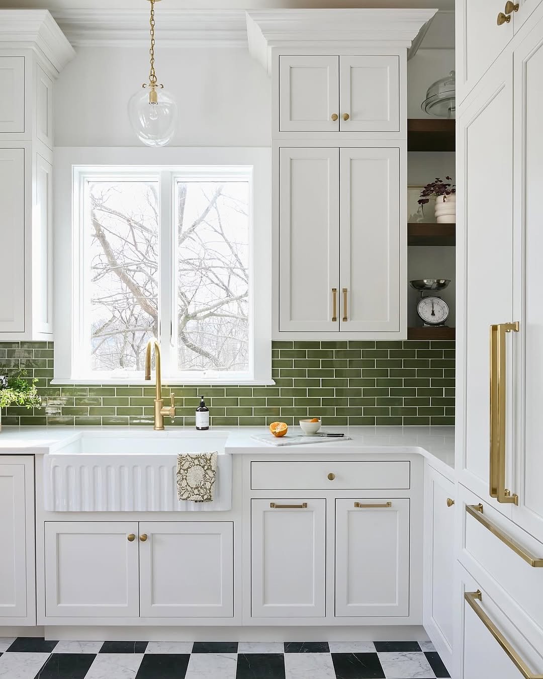 A bright white kitchen with a glossy, jewel-toned emerald green subway tile backsplash, contrasting with white shaker cabinets and brass hardware.