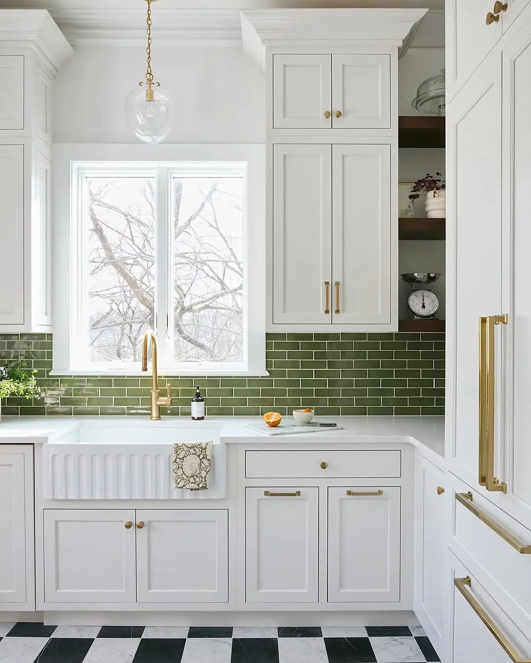 A bright white kitchen with a glossy, jewel-toned emerald green subway tile backsplash, contrasting with white shaker cabinets and brass hardware.