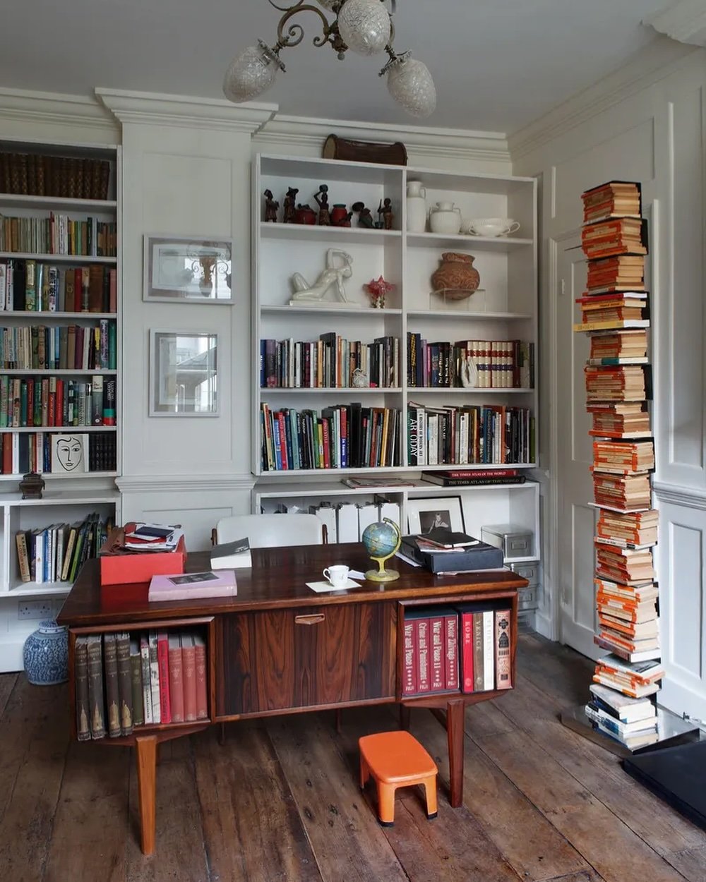 A classic mid-century modern study desk with a dark wood finish, open book storage, and an orange stool.